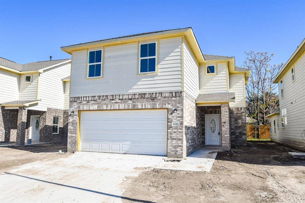 New two-story residential home with brick facade, white siding, and a two-car garage under a clear blue sky.