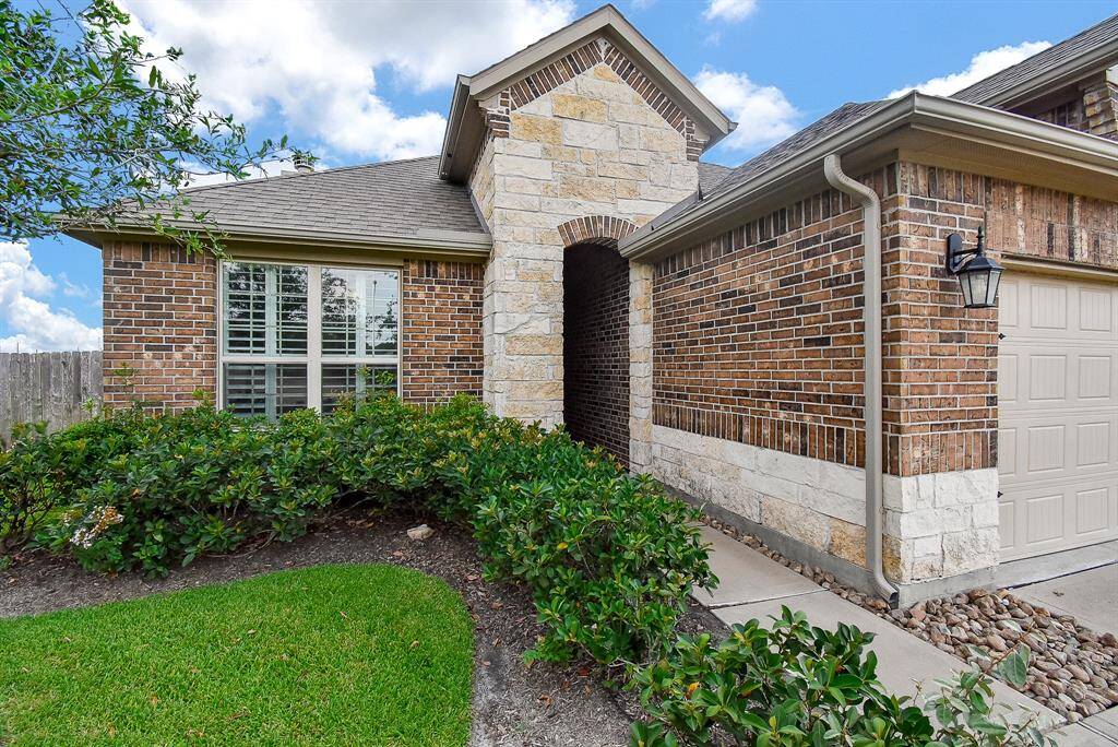 Single-story brick home featuring a prominent stone entry arch and well-manicured landscaping. Front yard maintenance by HOA.