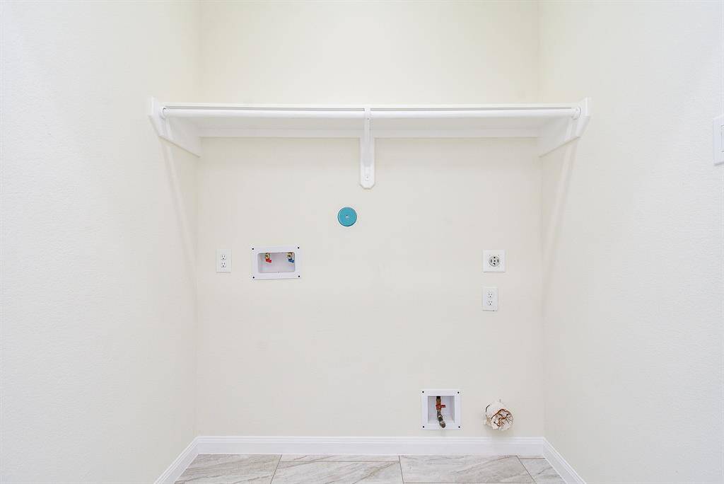 An empty closet space with a shelf, hook-ups for a washer and dryer, and various outlets on a wall.