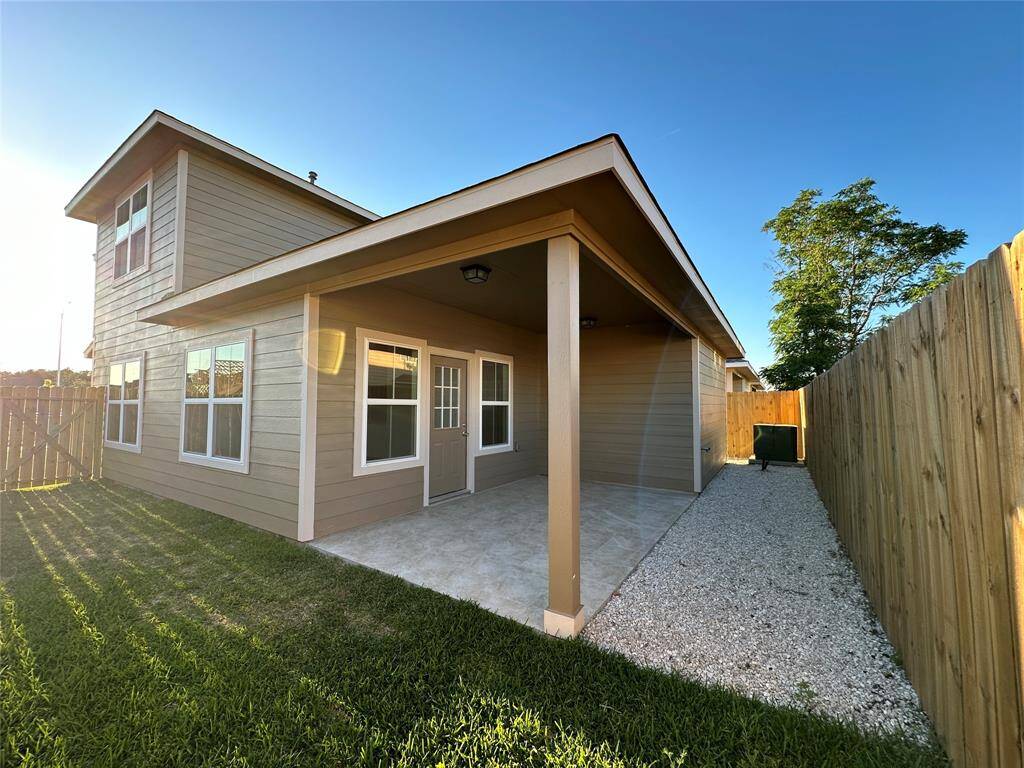 A two-story house with beige siding, a covered patio, and a wooden fence during sunset.