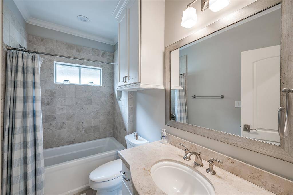 Guest bathroom features tub/shower with tile surround, tile flooring, stone countertops and cabinetry below, plus decorative mirror and light fixture.