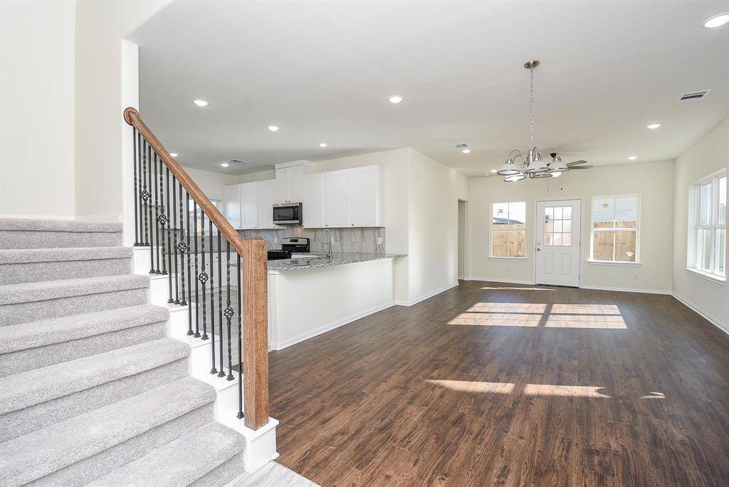 Bright, empty interior of a modern house with kitchen, staircase, hardwood floors, and chandelier.
