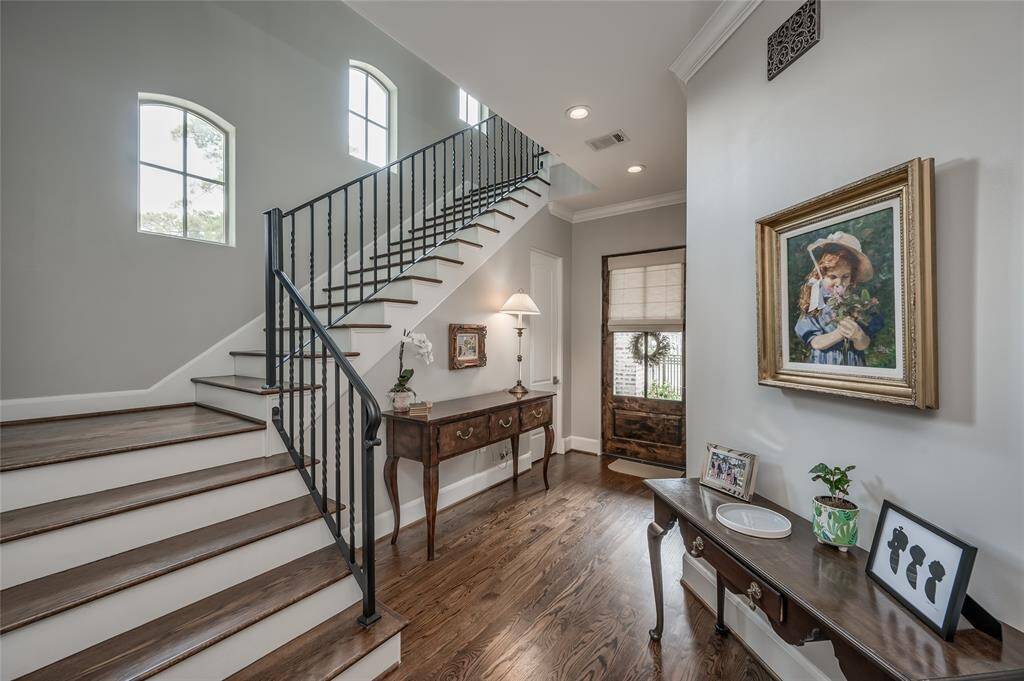 Warm and welcoming entry hall offers wooden stairs with iron railing, hardwood floors, crown moulding, recessed lightning, and walk-in wine bar.