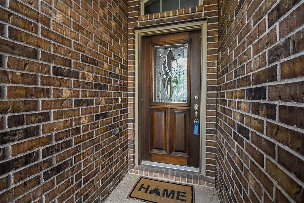 Cozy entryway featuring a classic wood front door with decorative glass, surrounded by a warm-toned brick exterior.