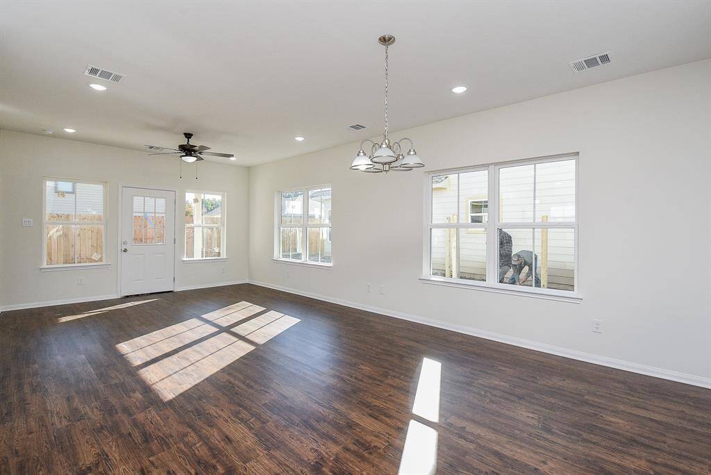 Empty room with hardwood floors, white walls, ceiling fans, and a dog looking through the glass door.