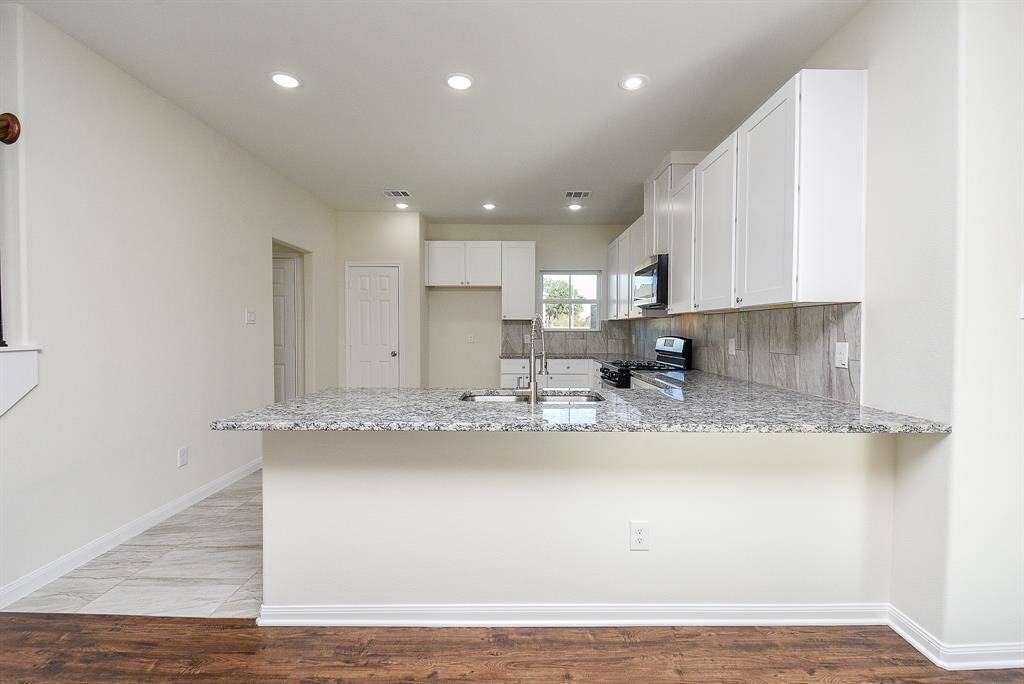 Modern kitchen with white cabinets, granite countertops, stainless steel appliances, and a mix of tile and hardwood flooring.