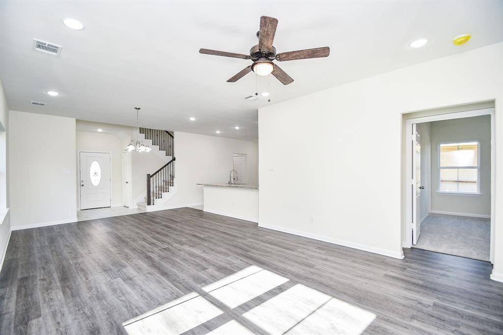 Empty modern room with wood flooring, white walls, chandelier, ceiling fan, and staircase leading to an upper level.
