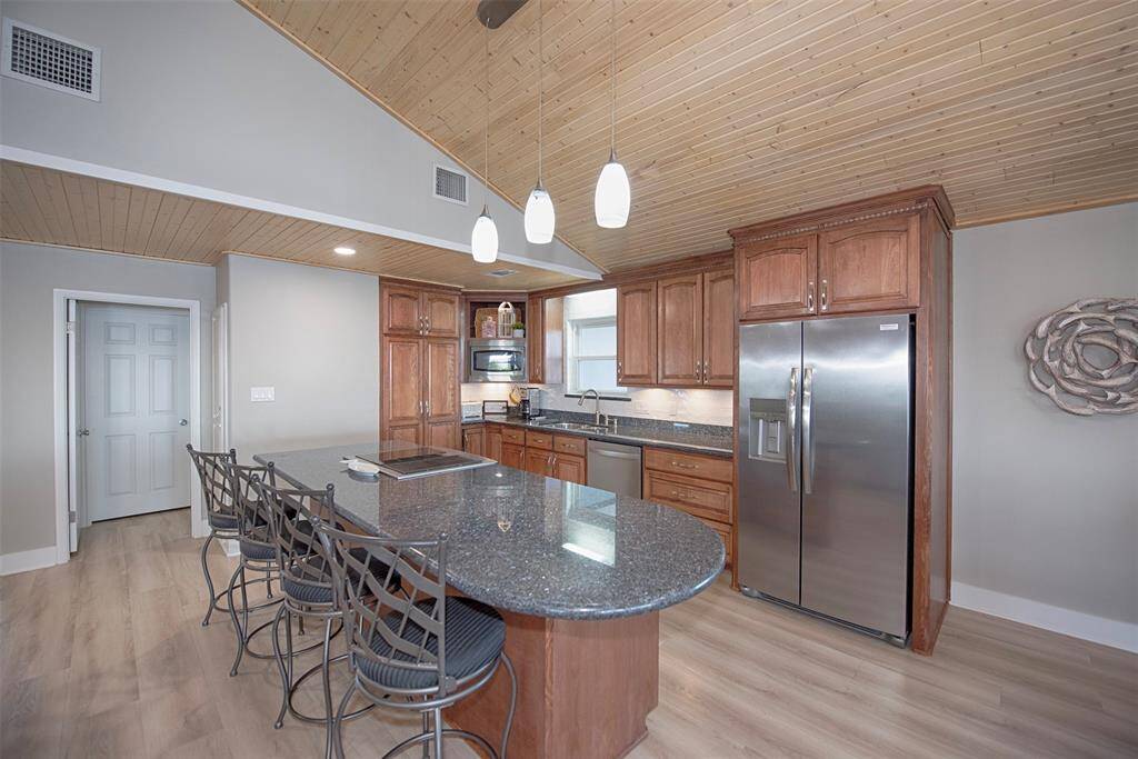 Elegant gourmet kitchen featuring a spacious wrap-around breakfast bar, stunning high wood ceiling, and ample storage and counter space.
