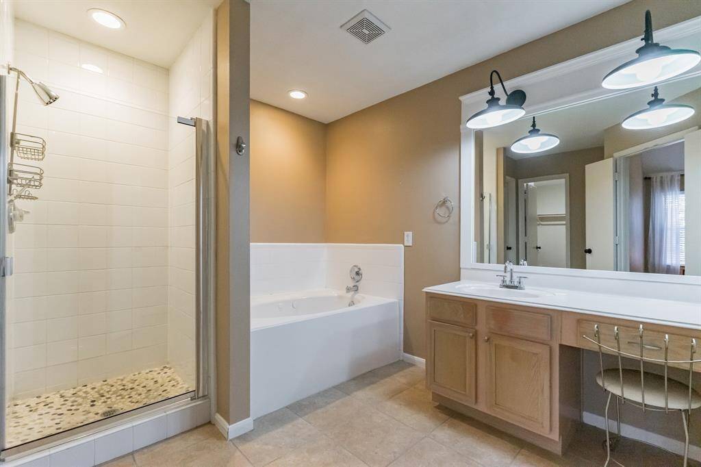 This primary bathroom features a spacious walk-in shower with a glass door, a large jetted soaking tub, and a vanity with ample counter space and stylish lighting. The neutral tones create a warm, inviting atmosphere.