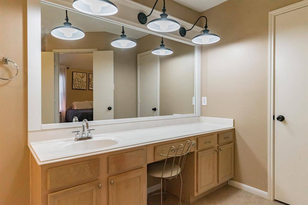 The secondary bathroom features a spacious vanity with ample countertop space and under-sink storage. It has an elegant mirror with modern lighting above.