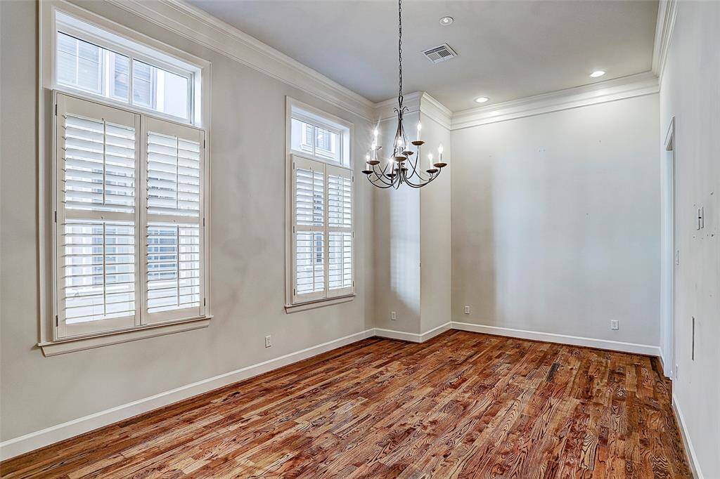 The sun-lit dining room epitomizes warmth coupled with elegance boasting gleaming hardwood floors, multi-piece molding, plantation shutter-dressed windows and decorative chandelier.