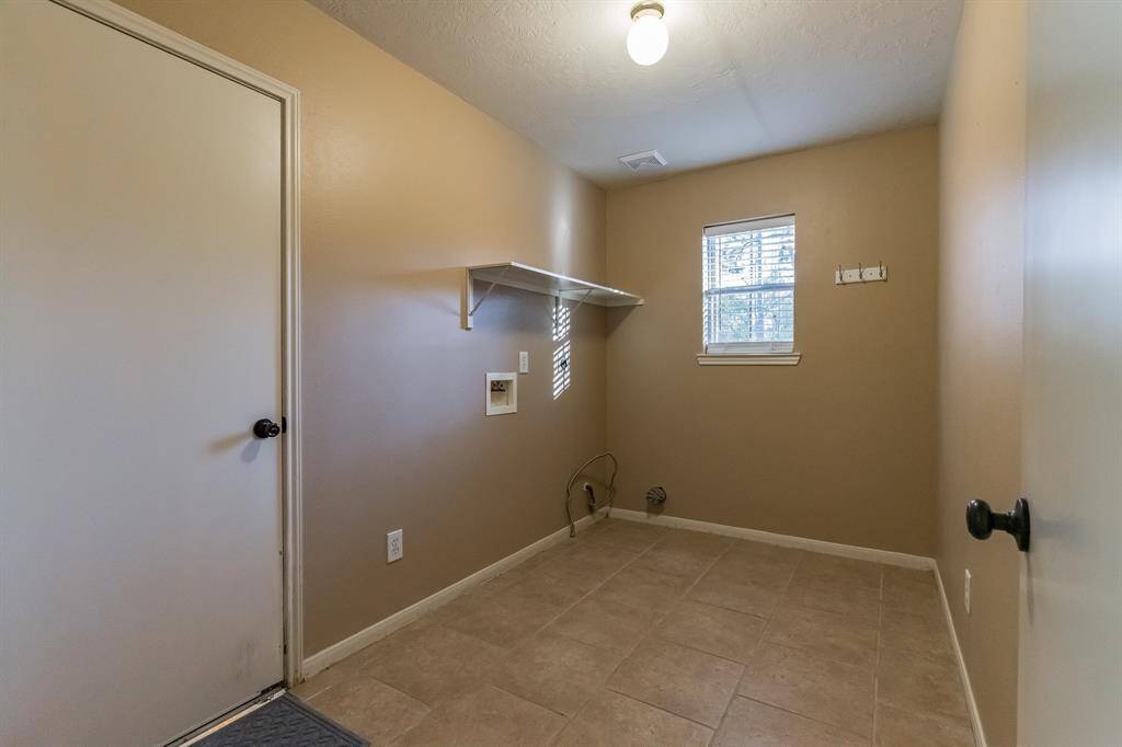 The utility room featuring neutral walls and tile flooring. It has a small window for natural light and a shelf for storage. Room for a stand up freezer as well.