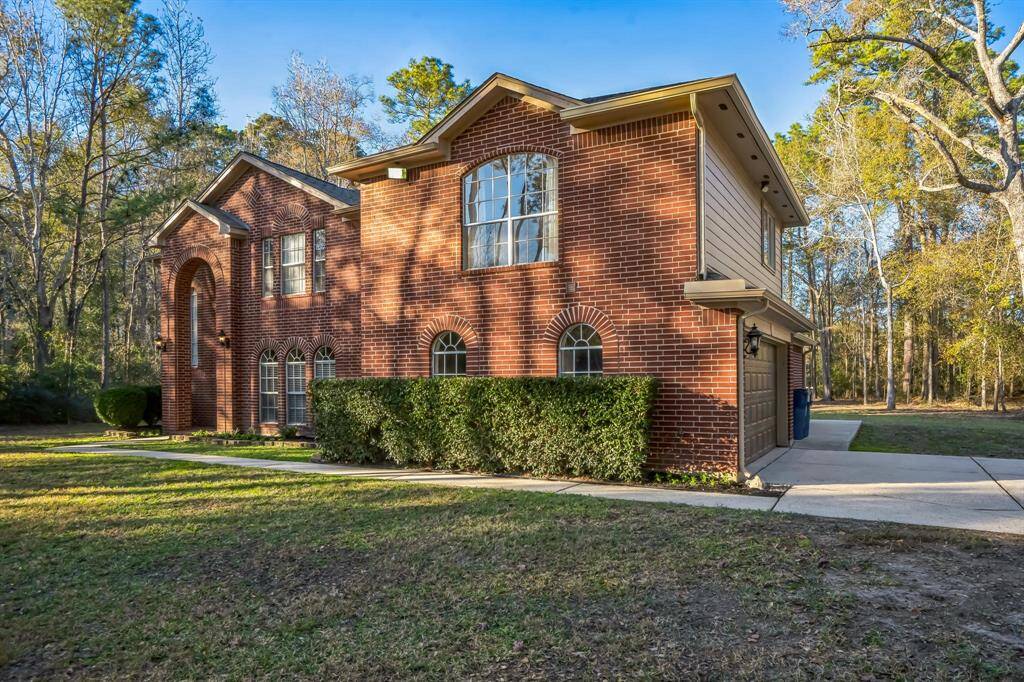 Lovely two-story brick home with a classic design, featuring large arched windows and a well-maintained front lawn and flower beds. The property is surrounded by mature trees, offering a serene and private setting. A paved driveway leads to the attached side load garage.