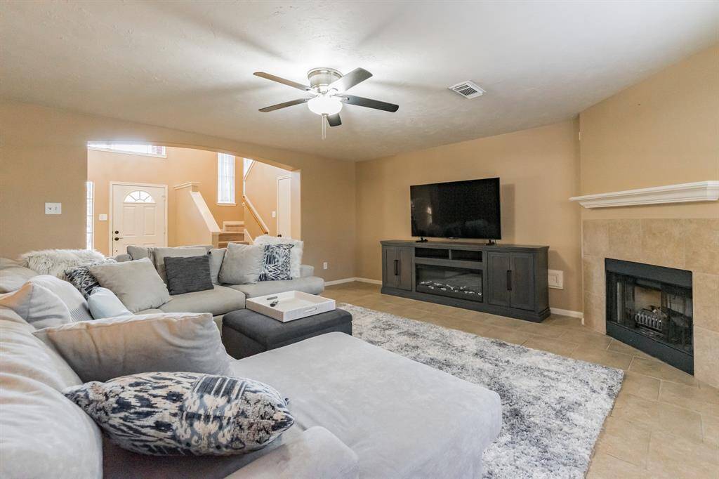 The open layout flows into the entryway, with a view of the staircase. Neutral tones and a ceiling fan enhance the comfortable atmosphere.