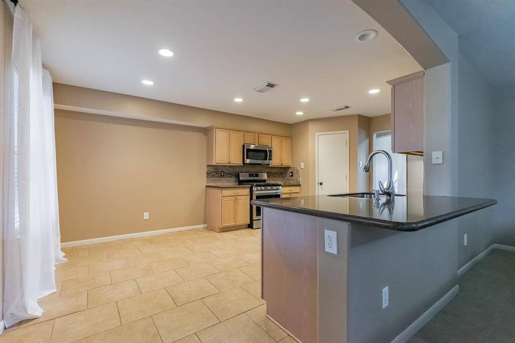 Bright and spacious kitchen with modern stainless steel appliances, ample cabinetry, and a sleek granite countertop. The open floor plan is enhanced by recessed lighting and tile flooring, creating a welcoming and functional space.