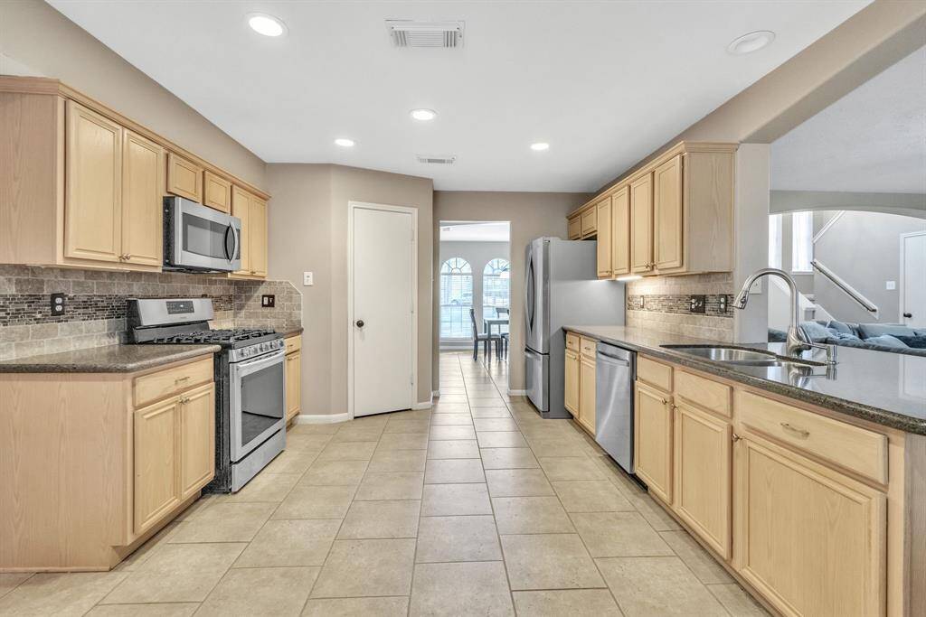 This spacious kitchen features light wood cabinetry, stainless steel appliances, and ample counter space. It opens to a dining area with large windows, offering plenty of natural light.