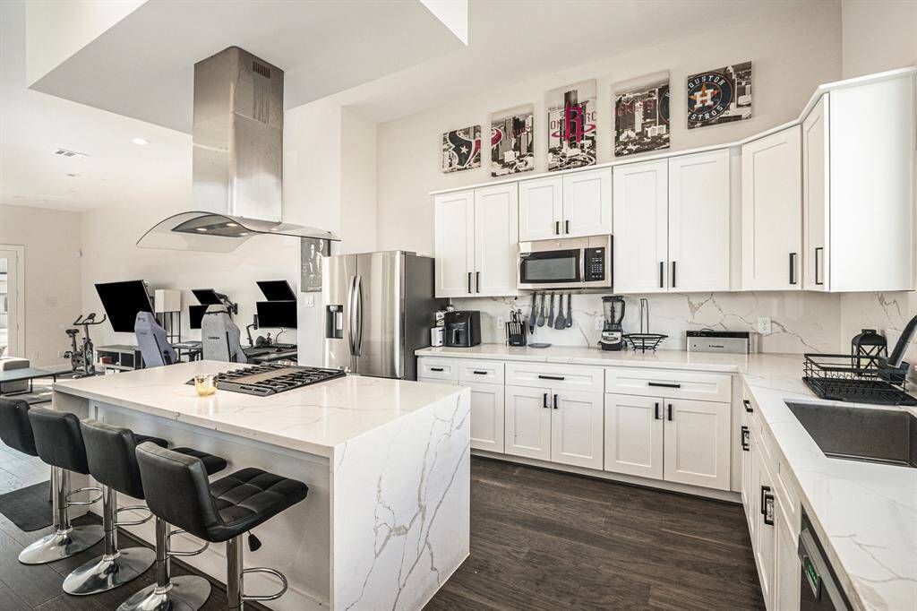 This modern kitchen features sleek white cabinetry, stainless steel appliances, and a spacious island with bar seating. The open layout connects to a bright area.
