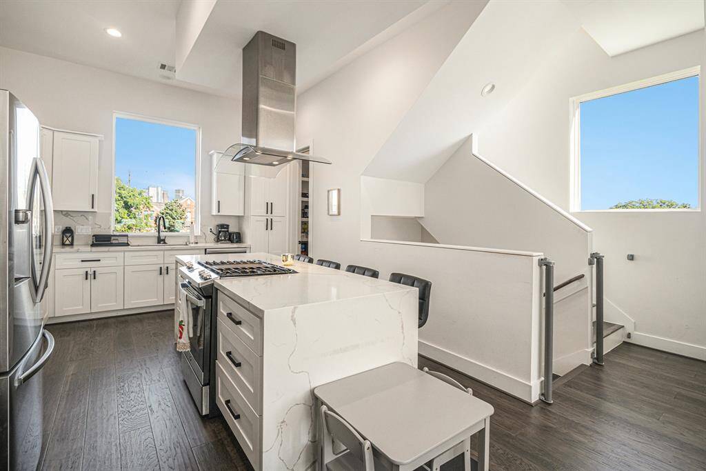 Bright, modern kitchen with white cabinetry, sleek appliances, and a large island with seating. High ceilings and ample natural light create an open, airy feel.