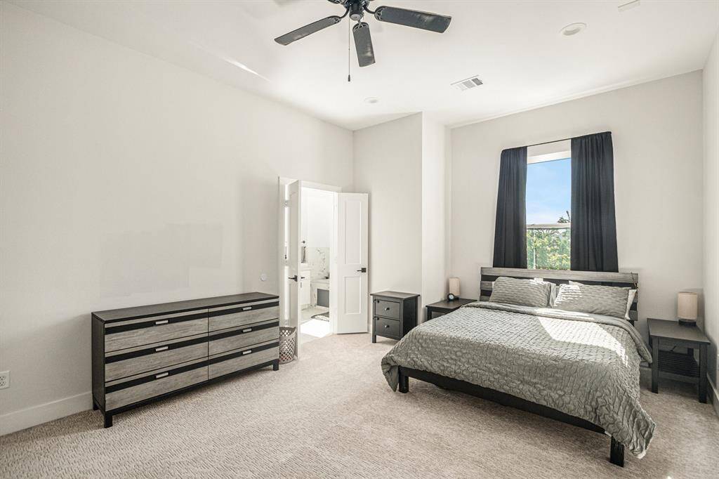 This bright bedroom features a modern design with a neutral color palette, large window for natural light, a ceiling fan, and an en-suite bathroom for convenience.