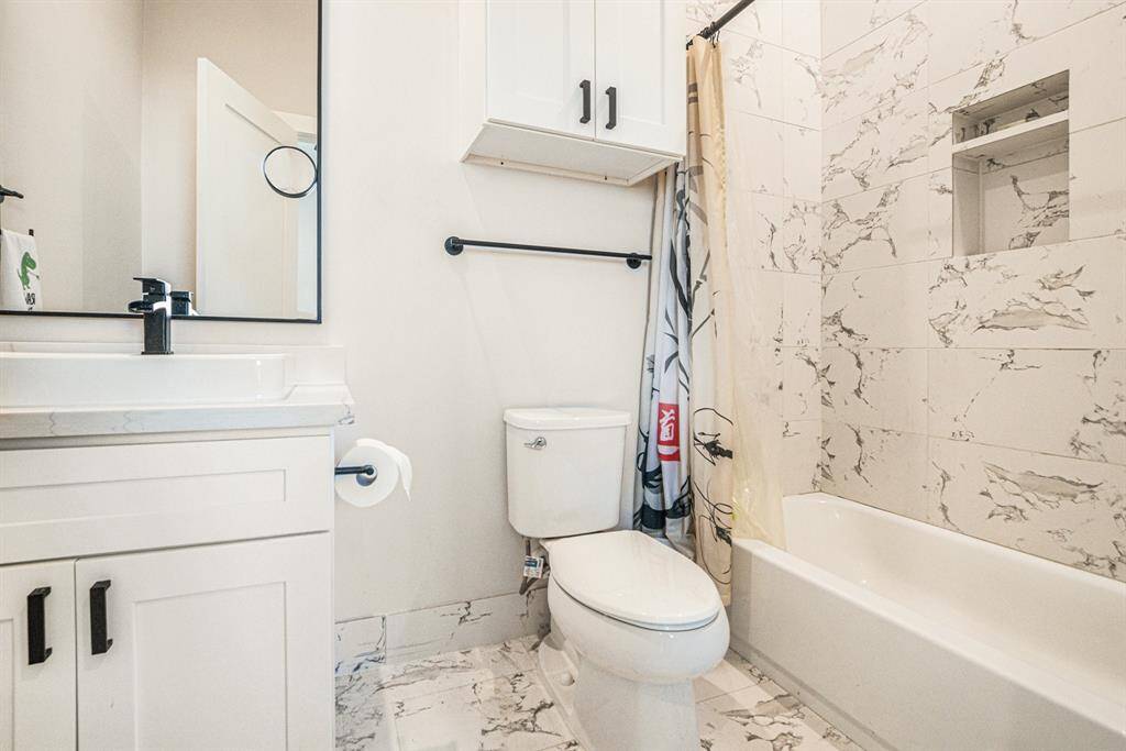 This bathroom features a clean, modern design with white cabinetry, a sleek vanity, and a bathtub surrounded by elegant marbled tile.