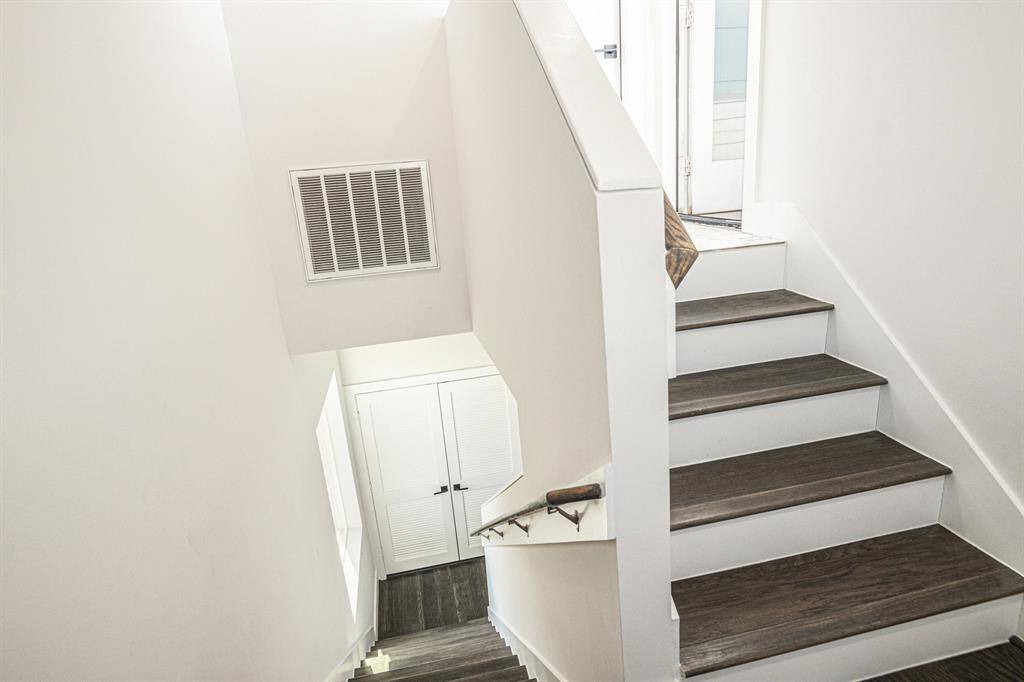 This photo shows a modern stairway with dark wood steps and white walls, leading to a bright area at the top with an amazing view of Downtown Houston.