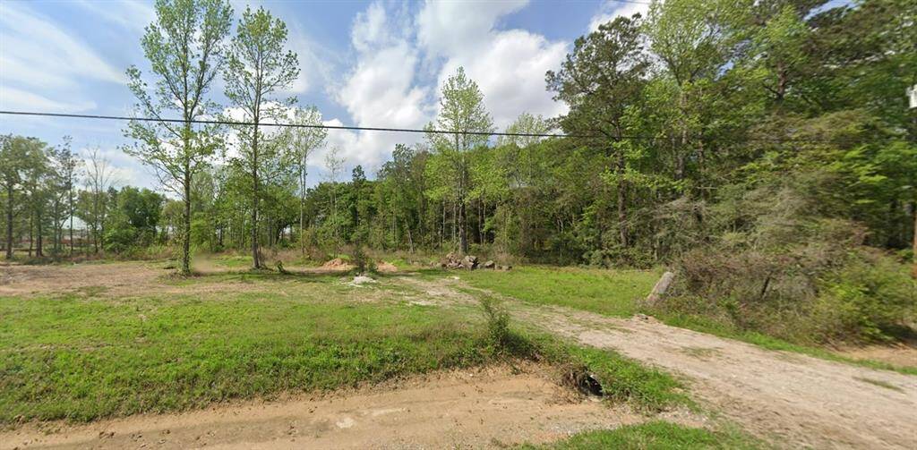 This photo shows a spacious, grassy lot with a few trees and a dirt path. It's surrounded by a wooded area, offering plenty of privacy and natural scenery. Ideal for buyers seeking a serene, rural setting.