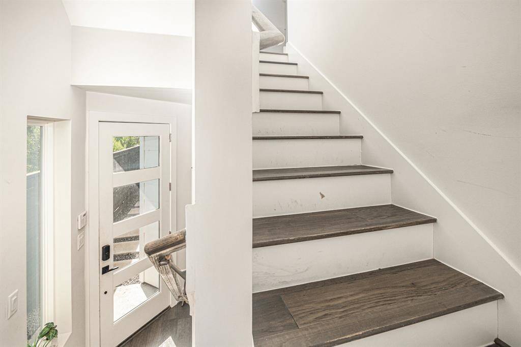 This photo showcases a modern staircase with dark wood steps and white risers, leading up from a bright entryway. Head upstairs to the mail living.