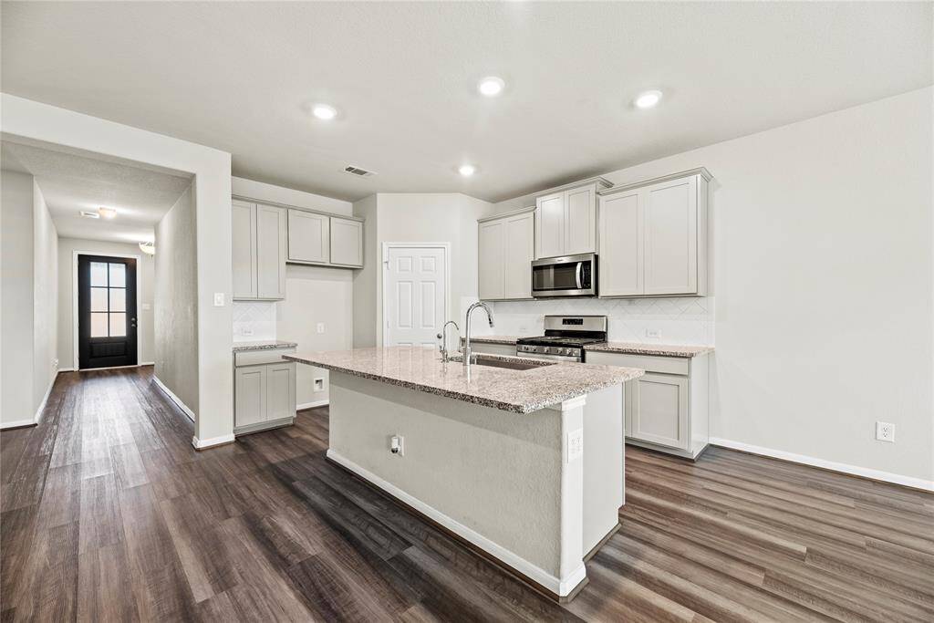 Your kitchen features include quartz countertops paired with a coordinating tile backsplash, stainless steel appliances, crisp white cabinets, recessed lighting, and a sprawling island with breakfast bar seating.