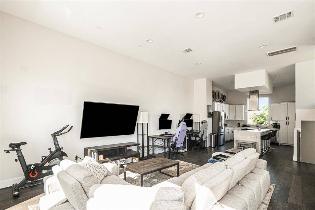 This modern open-concept living area features a spacious layout.   The area seamlessly flows into a sleek kitchen with stainless steel appliances and a breakfast bar. High ceilings and ample natural light enhance the inviting atmosphere.