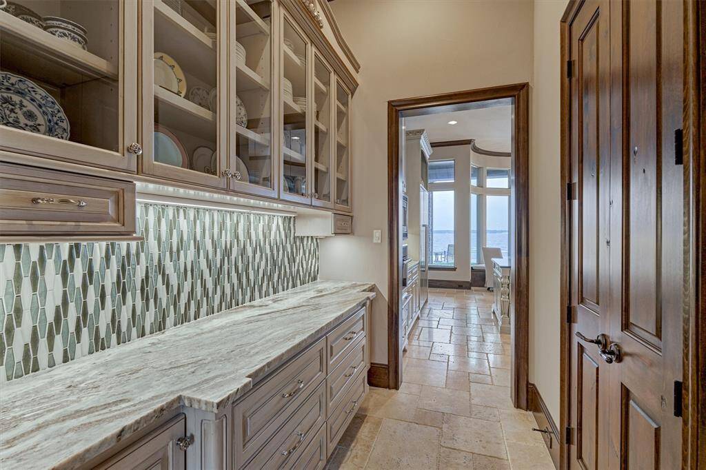 The butler's pantry connects the kitchen to the formal dining room and features glass front cabinets, a striking backsplash, and a leathered granite countertop. Adjacent to it is a spacious walk-in pantry providing more counter space and ample storage for food and smaller appliances.
