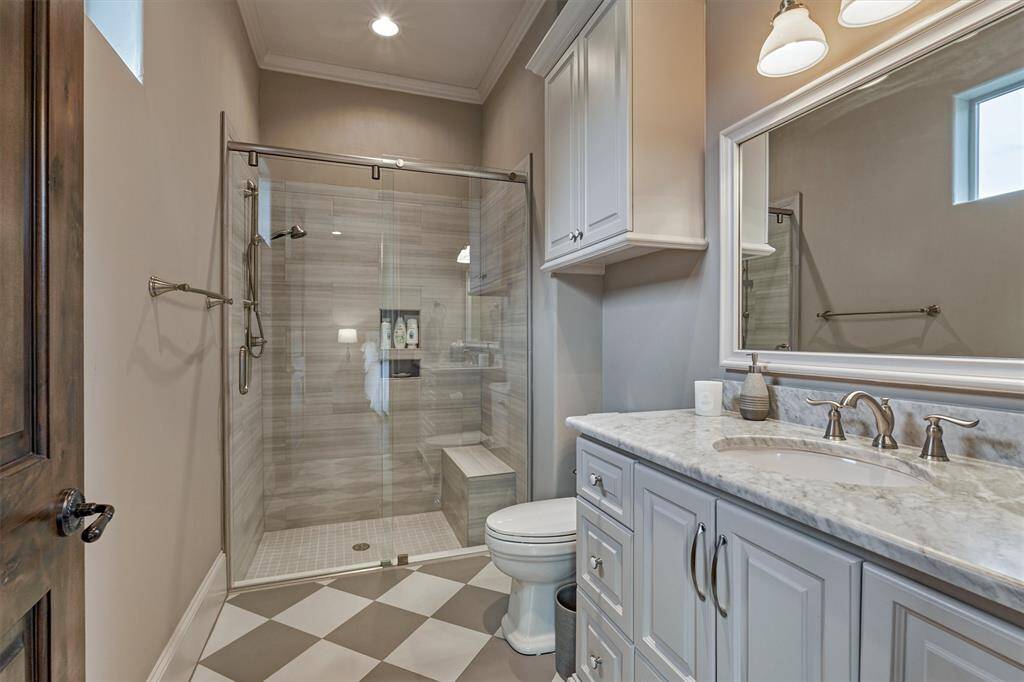 The ensuite bath for the first floor guest bedroom has an eye-catching checkered floor tile design, seamless glass shower with bench and a great amount of cabinet and counter space.