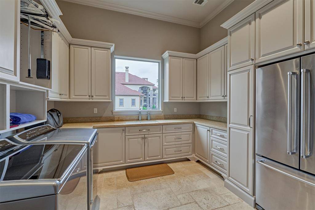 The spacious laundry room is equipped with folding counters, storage cabinets, a sink, and fridge space.