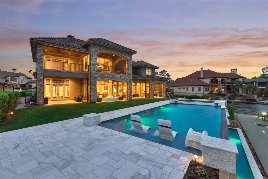 The view of the home at night captures the lighting in covered back porch spaces as well as the lighting in the pool and the marble tile surrounding the pool.