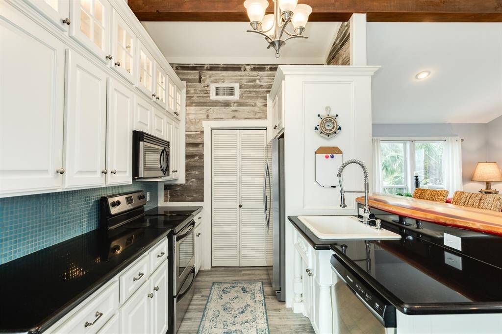 The black granite countertops & glass tile backsplash add striking color contrast to the main area of the home. The louvered bifold doors in view lead into the utility/pantry storage room.
