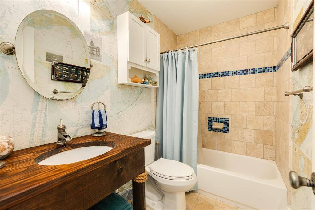 Hall bathroom on the main level of home is located between bedrooms 1 & 2. Repurposed table used as a vanity, natuical charts applied as wall covering, with a tub/shower arrangement.
