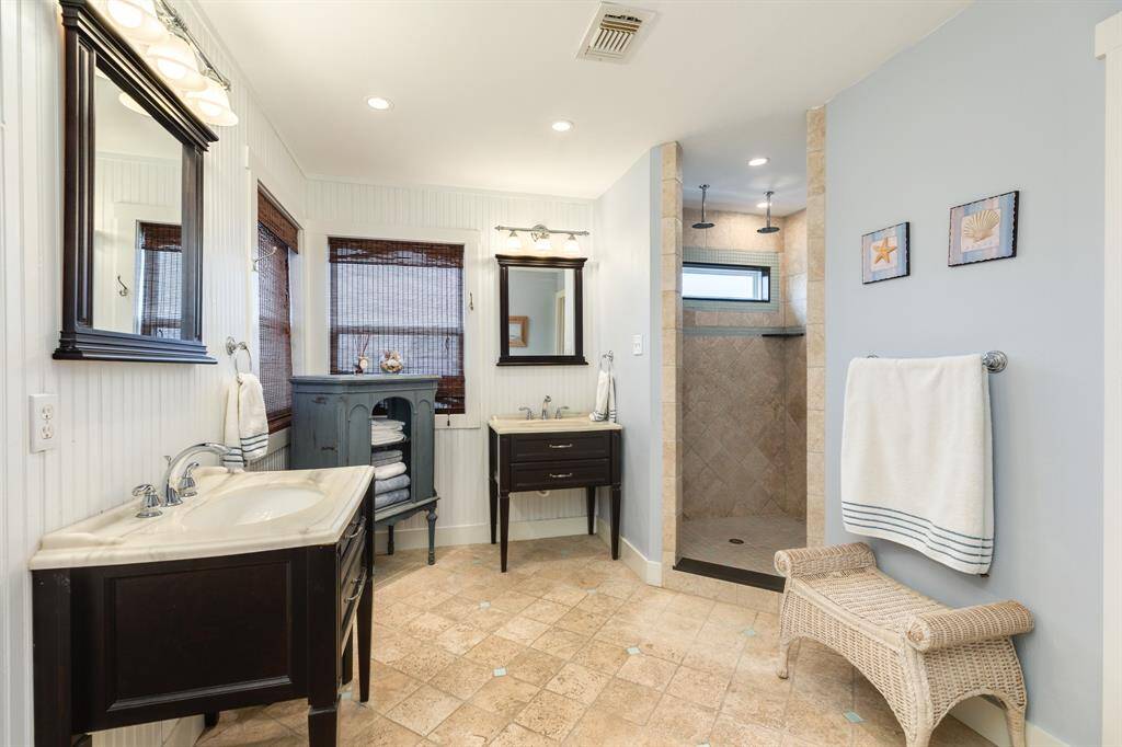 Spacious primary bath with custom vanity sinks, walk in shower and seating area.