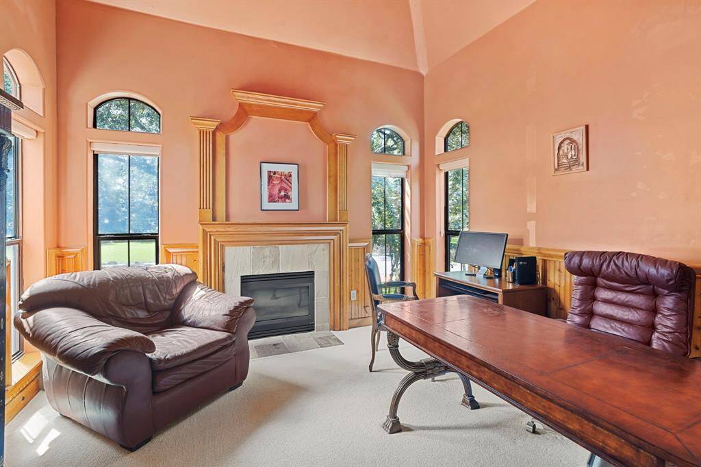 The study is privately located on the mezzanine between the first and second floors and features a central gas-log fireplace, large windows with arched transoms, solid pine wainscoting, and built-in custom cabinetry.