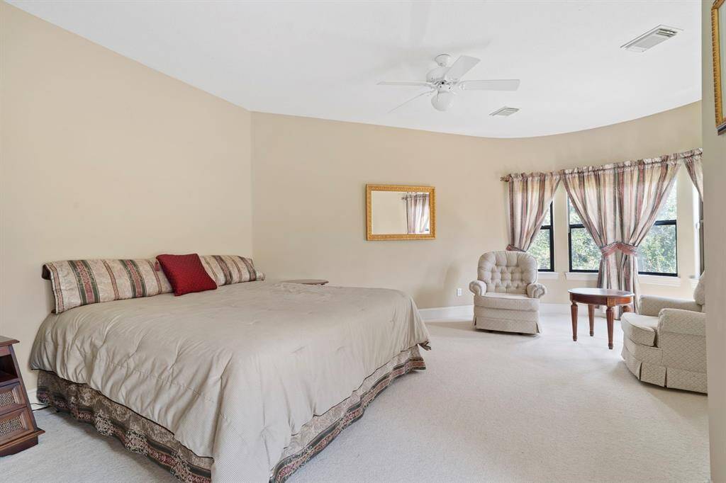 This spacious bedroom features a sitting area, en suite Hollywood bathroom, and French doors to an exterior balcony overlooking the pool.