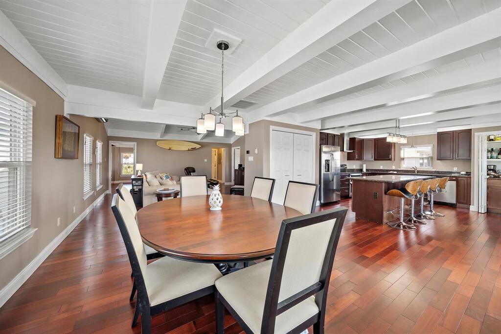Seamless flow from the elegant dining area to the gourmet kitchen, perfect for hosting. Note the coffered ceiling beams and expansive layout, blending comfort with functionality in a beautifully updated coastal interior.