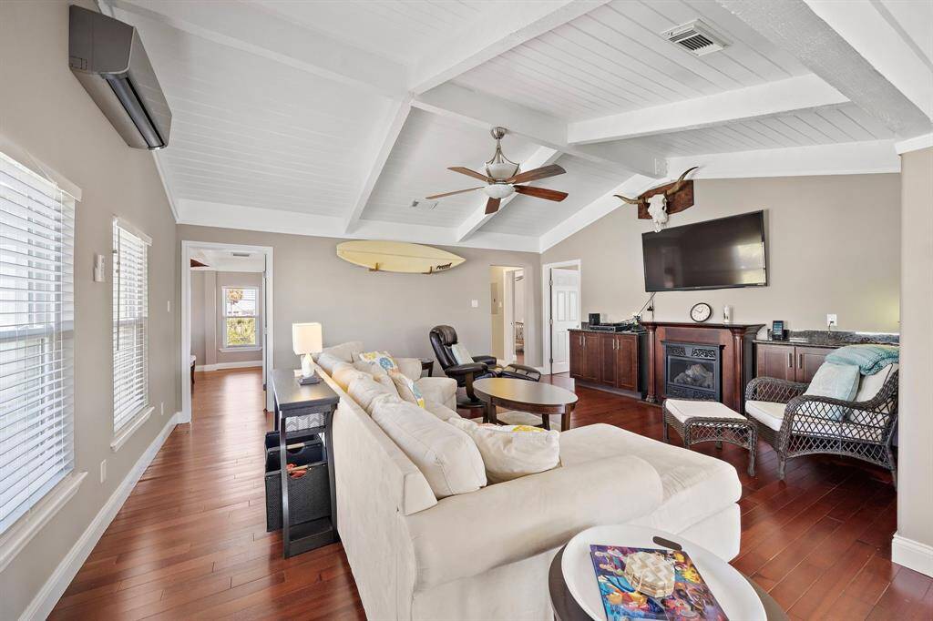 A warm and inviting living room with vaulted ceilings and wood floors, centered around a stylish entertainment setup and electric fireplace. The mounted TV, cozy seating, and tasteful decor make this an ideal space to unwind after a day on the water.