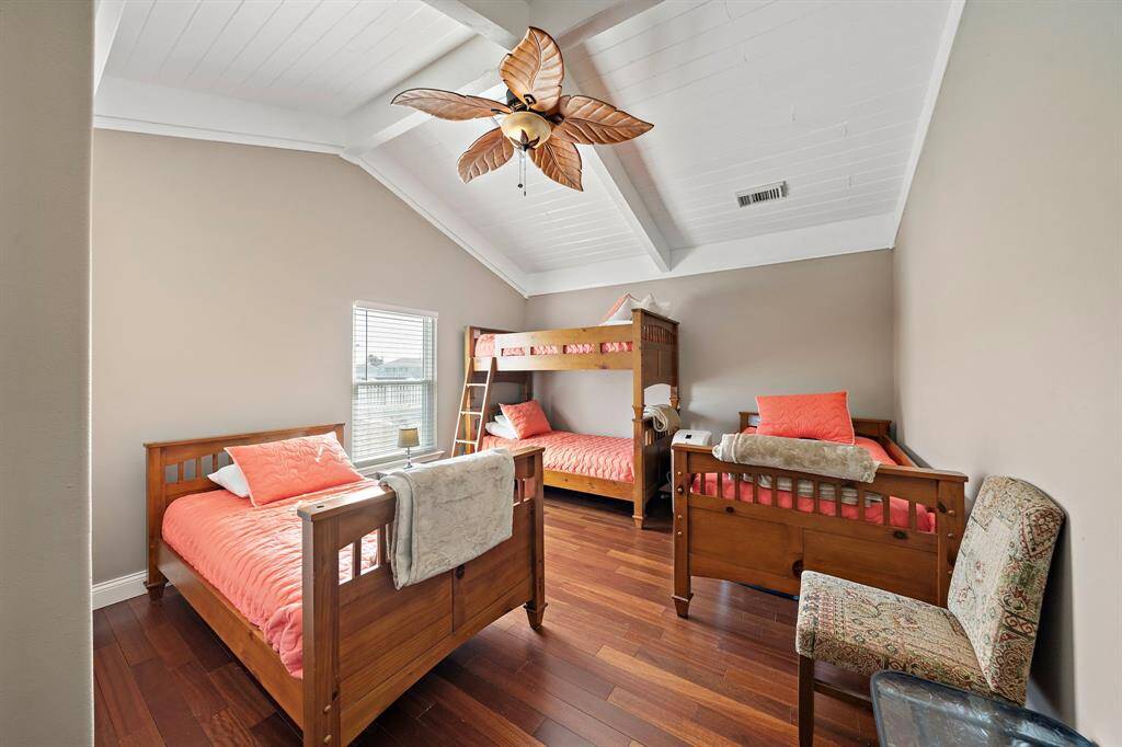 Perfect for accommodating guests or family, this spacious bedroom is outfitted with two twin beds and a bunk bed. Vaulted ceilings with exposed beams and a fun, tropical ceiling fan complete the playful yet refined atmosphere.