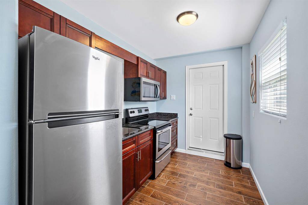 View from the opposite side of the kitchen, showing a clean and functional space with natural light, durable wood-look tile flooring, and modern amenities.