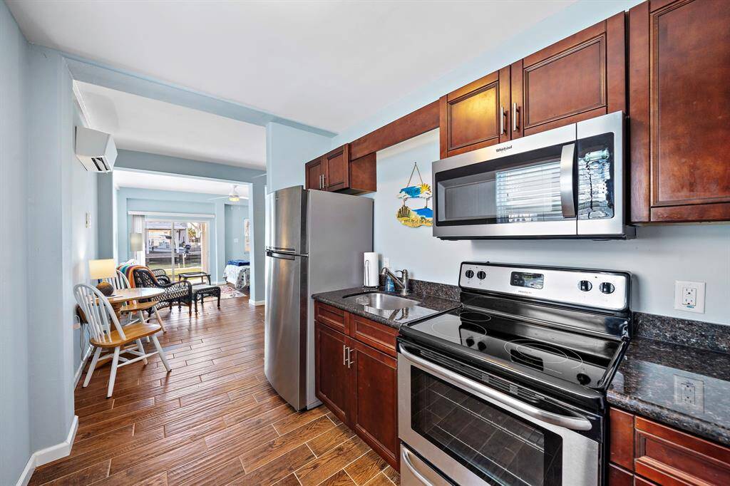 A compact but fully equipped kitchen with stainless steel appliances, granite countertops, and dark wood cabinetry. The open layout flows easily into the rest of the in-law suite’s living space.