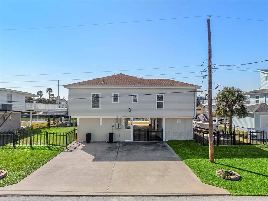 Well-maintained exterior with a wide driveway and gated entry to a carport underneath the home. Elevated construction provides covered parking and additional storage, while the manicured lawn and fencing enhance curb appeal and security.