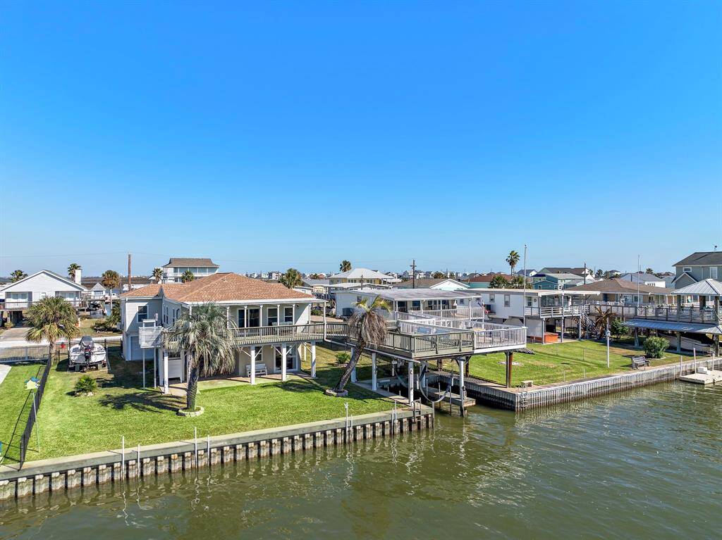 An angled aerial shot showing the home, boat dock, and neighboring properties along the canal. This perspective captures how the property is nestled in a quiet, open stretch of water with direct boating access and minimal obstruction.
