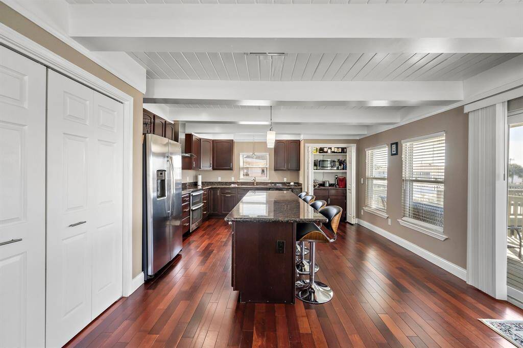 A chef’s dream kitchen featuring rich wood cabinetry, granite countertops, stainless steel appliances, and a spacious island with bar seating. The open-concept design is perfect for entertaining, all while enjoying natural light and water views through the surrounding windows.