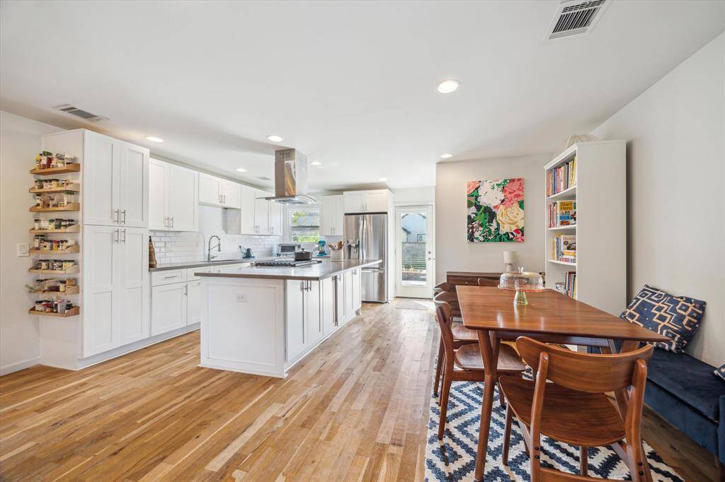 The kitchen is lined with abundant storage cabinets, coordinating subway tile backsplash, and stainless steel appliances, creating a bright and clean aesthetic. The kitchen island provides additional storage space, as well as convenient breakfast bar seating.