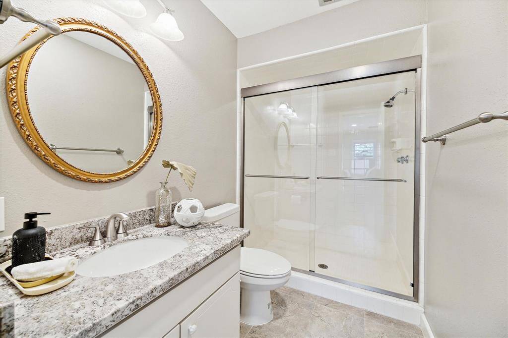 Ensuite bath with granite counters a stylish mirror and a glass enclosed shower.