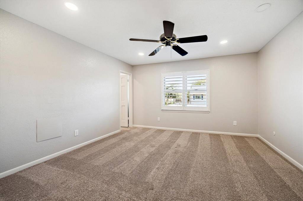 Spacious secondary bedroom with a walk-in closet, ensuite bath, LED recessed lights, ceiling fan and a large window with plantation shutters.
