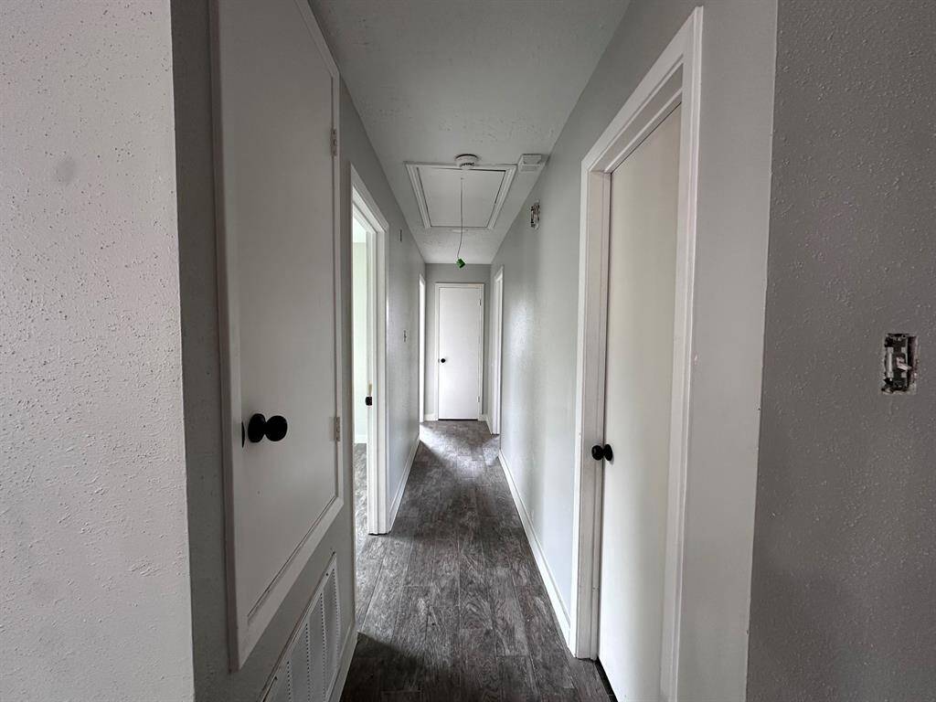 This is a hallway with light gray walls and dark wood flooring. It features multiple white doors with black knobs, leading to various rooms. The space is clean and well-lit.